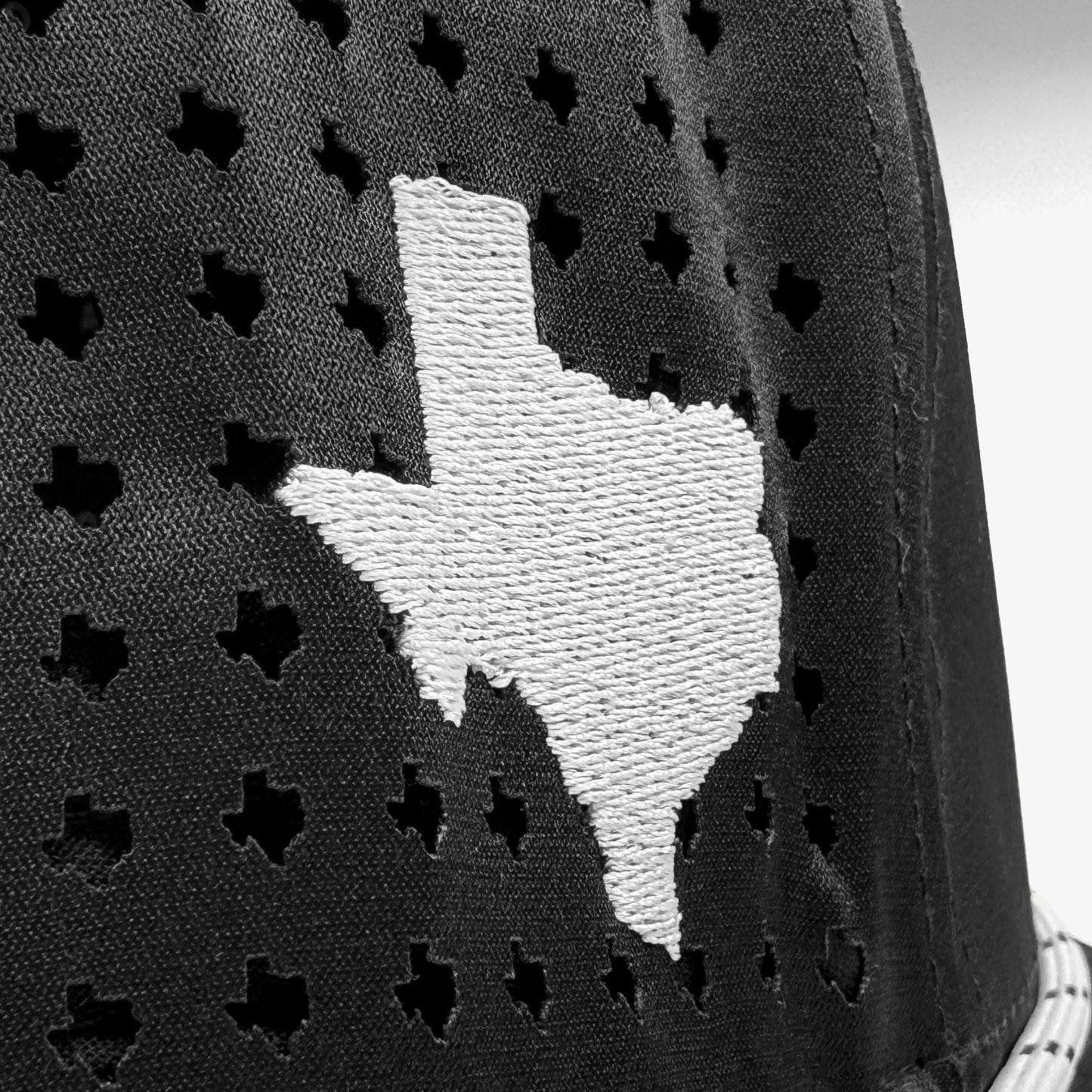 Black cap with white embroidered Texas shape on a textured background